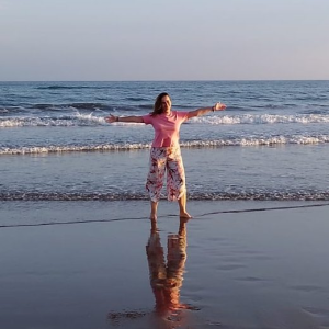Mujer con los brazos abiertos en la orilla del mar, postura de apertura y calma.