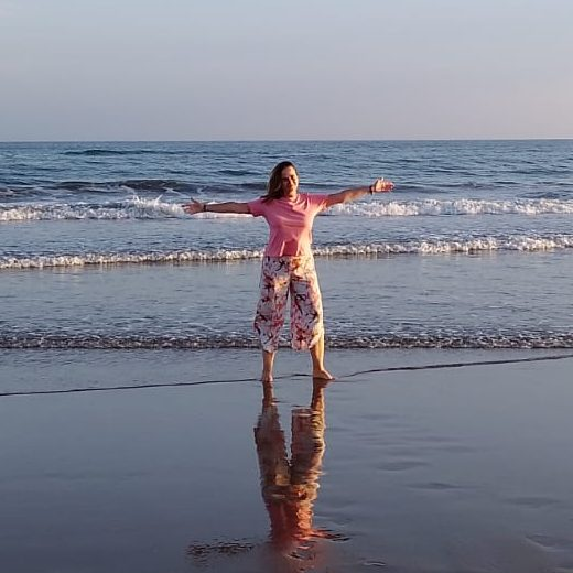 Mujer con los brazos abiertos en la orilla del mar, postura de apertura y calma.